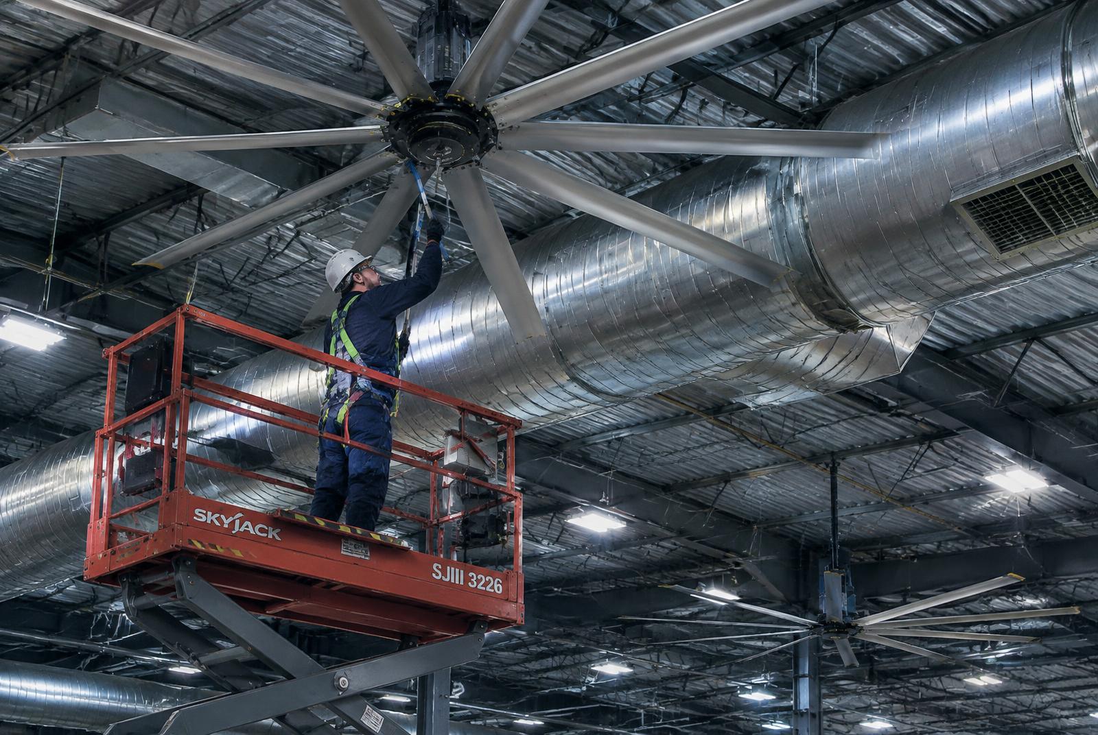 Worker on a lift cleaning high-bay fans